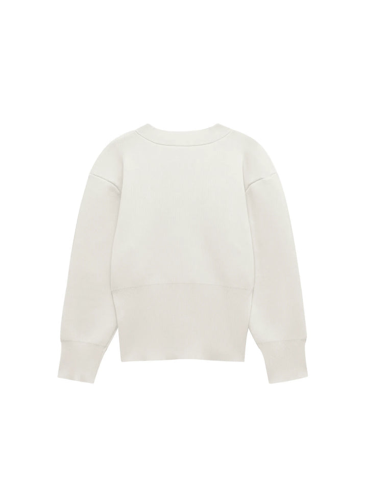 Model wearing a V-neck knit cardigan over a white tank top and trousers, enjoying a coffee outdoors in spring.