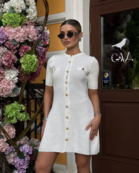 Confident woman walking downtown in a fitted ribbed knit mini dress with metal buttons, styled with sunglasses and ankle boots.