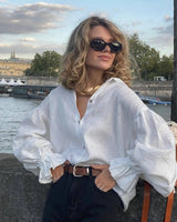 Model wearing white puff sleeve blouse with denim shorts, standing outdoors on a sunny day.
