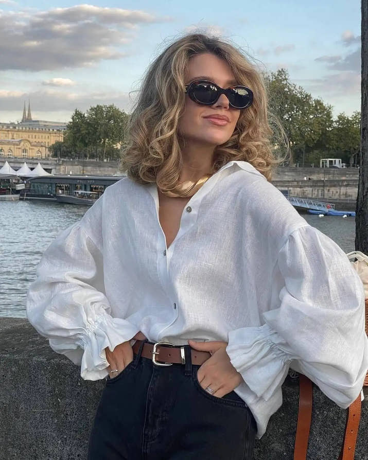 Model wearing white puff sleeve blouse with denim shorts, standing outdoors on a sunny day.