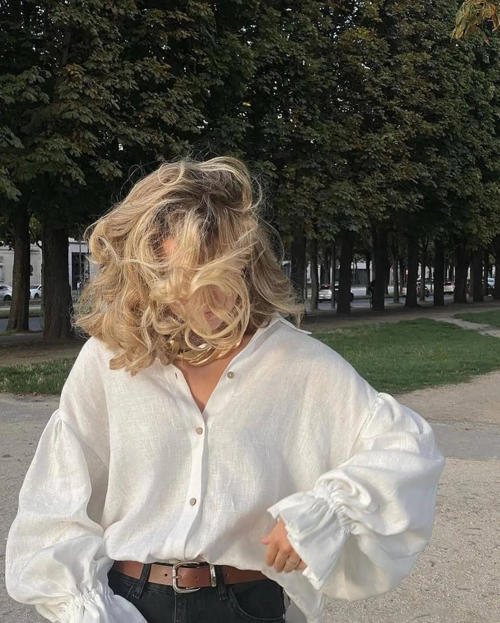 Model wearing white puff sleeve blouse with denim shorts, standing outdoors on a sunny day.