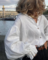 Model wearing white puff sleeve blouse with denim shorts, standing outdoors on a sunny day.