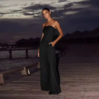 Woman wearing a strapless wide-leg backless jumpsuit, walking along a beach boardwalk at sunset, exuding effortless summer elegance.