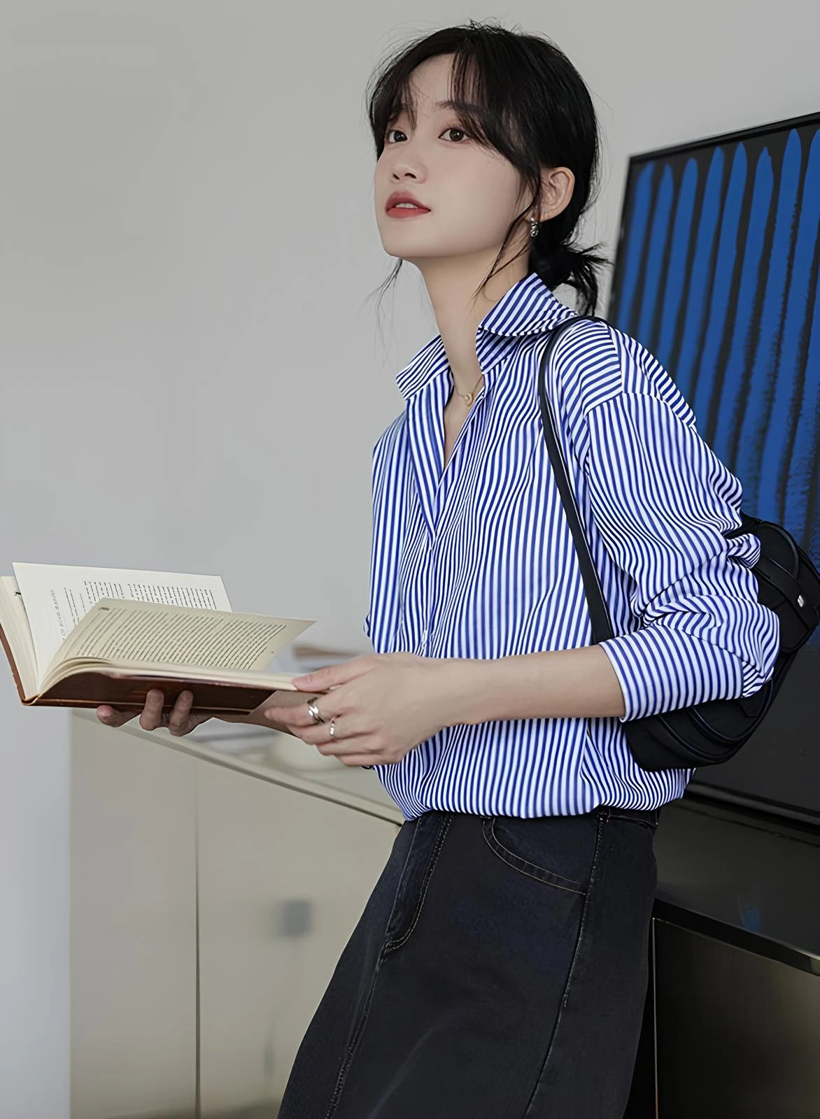Woman wearing a blue-white striped loose office shirt with lantern sleeves in a minimalist urban setting.