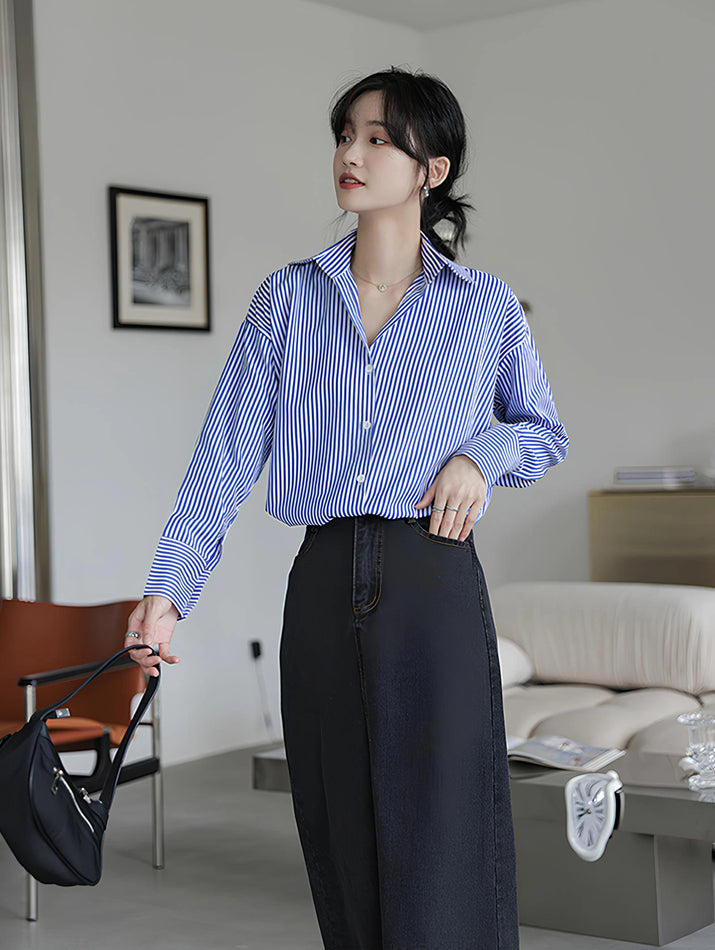 Woman wearing a blue-white striped loose office shirt with lantern sleeves in a minimalist urban setting.