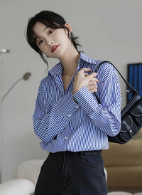 Woman wearing a blue-white striped loose office shirt with lantern sleeves in a minimalist urban setting.