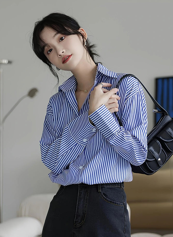 Woman wearing a blue-white striped loose office shirt with lantern sleeves in a minimalist urban setting.