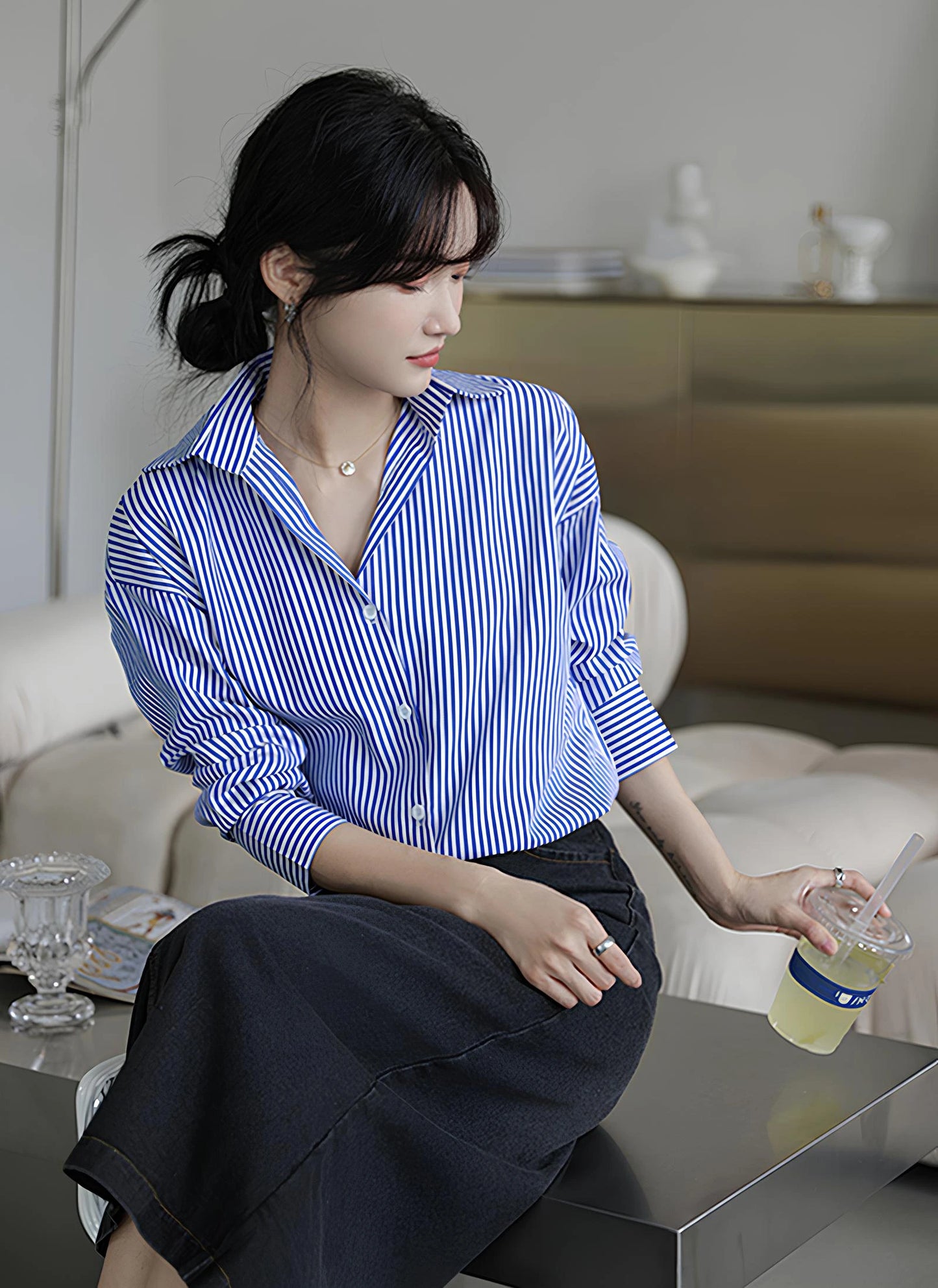 Woman wearing a blue-white striped loose office shirt with lantern sleeves in a minimalist urban setting.