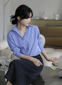 Woman wearing a blue-white striped loose office shirt with lantern sleeves in a minimalist urban setting.