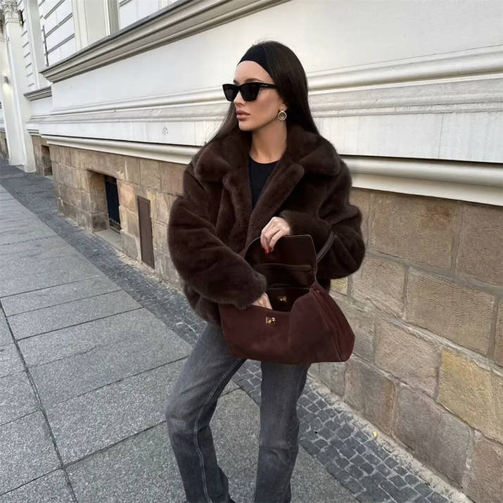 Woman wearing a brown faux fur winter jacket while sipping coffee outside a cozy café in cold weather.