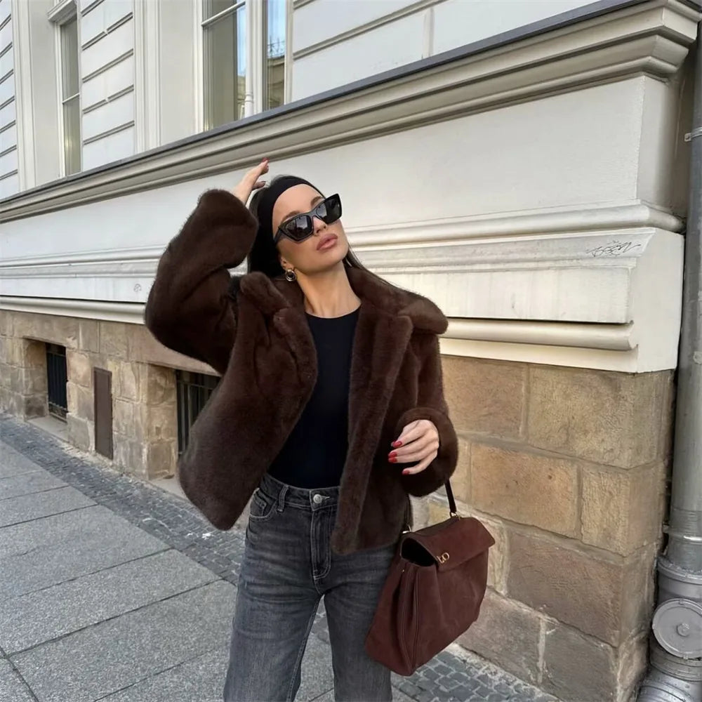 Woman wearing a brown faux fur winter jacket while sipping coffee outside a cozy café in cold weather.