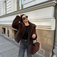 Woman wearing a brown faux fur winter jacket while sipping coffee outside a cozy café in cold weather.