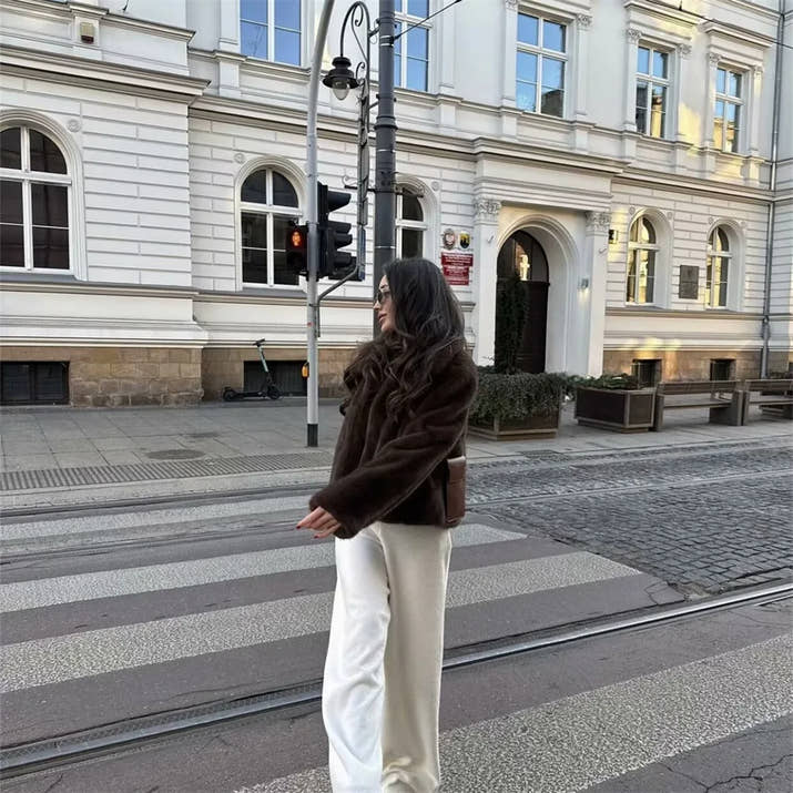 Woman wearing a brown faux fur winter jacket while sipping coffee outside a cozy café in cold weather.