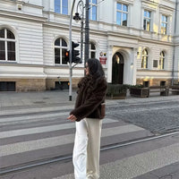 Woman wearing a brown faux fur winter jacket while sipping coffee outside a cozy café in cold weather.