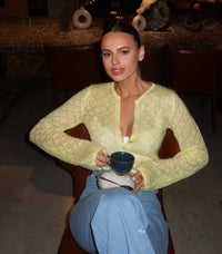 Woman in a yellow sweater holding a blue mug in a dimly lit room.