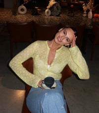 Woman wearing a hollow-out white knit cardigan over casual spring outfit in bright outdoor setting.