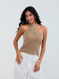 Model wearing khaki cross-front knit tank top with white cargo pants and sneakers, walking through a sunny urban street.