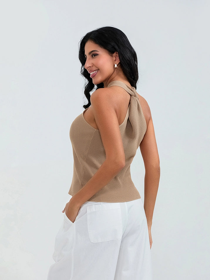 Model wearing khaki cross-front knit tank top with white cargo pants and sneakers, walking through a sunny urban street.