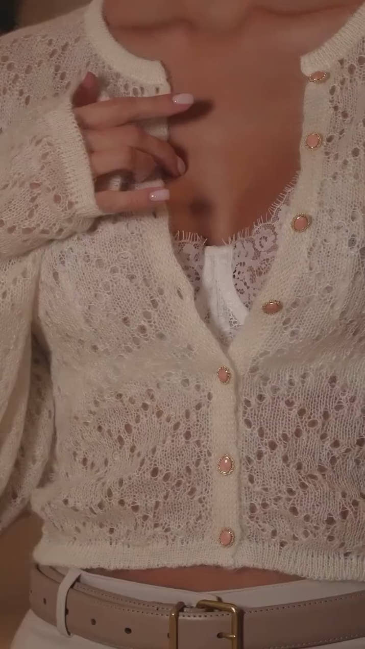 Woman wearing a hollow-out white knit cardigan over casual spring outfit in bright outdoor setting.