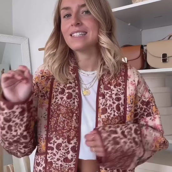 Woman walking outdoors in fall wearing a quilted patchwork floral jacket in orange tones.