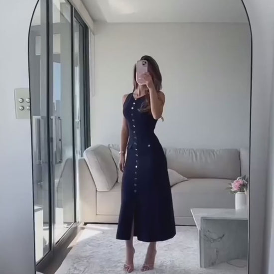 Elegant woman walking on a spring evening street in a sleeveless ribbed white maxi dress with gold buttons and heels.