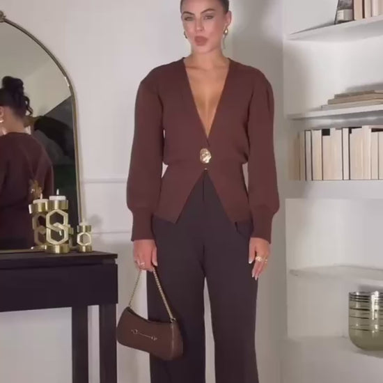 Model wearing a V-neck knit cardigan over a white tank top and trousers, enjoying a coffee outdoors in spring.