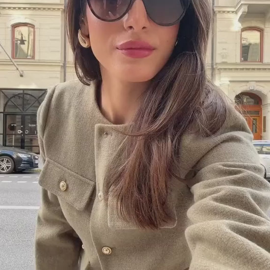 The woman looks casual and chic while walking around the city in a lightly cut khaki double-breasted tweed jacket with buttons.