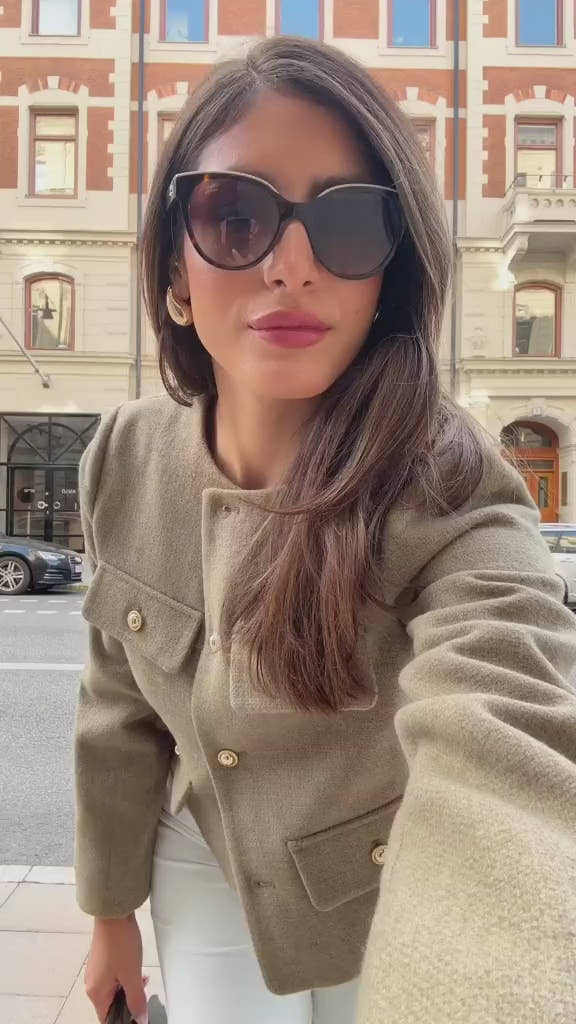 The woman looks casual and chic while walking around the city in a lightly cut khaki double-breasted tweed jacket with buttons.