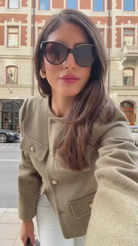 The woman looks casual and chic while walking around the city in a lightly cut khaki double-breasted tweed jacket with buttons.